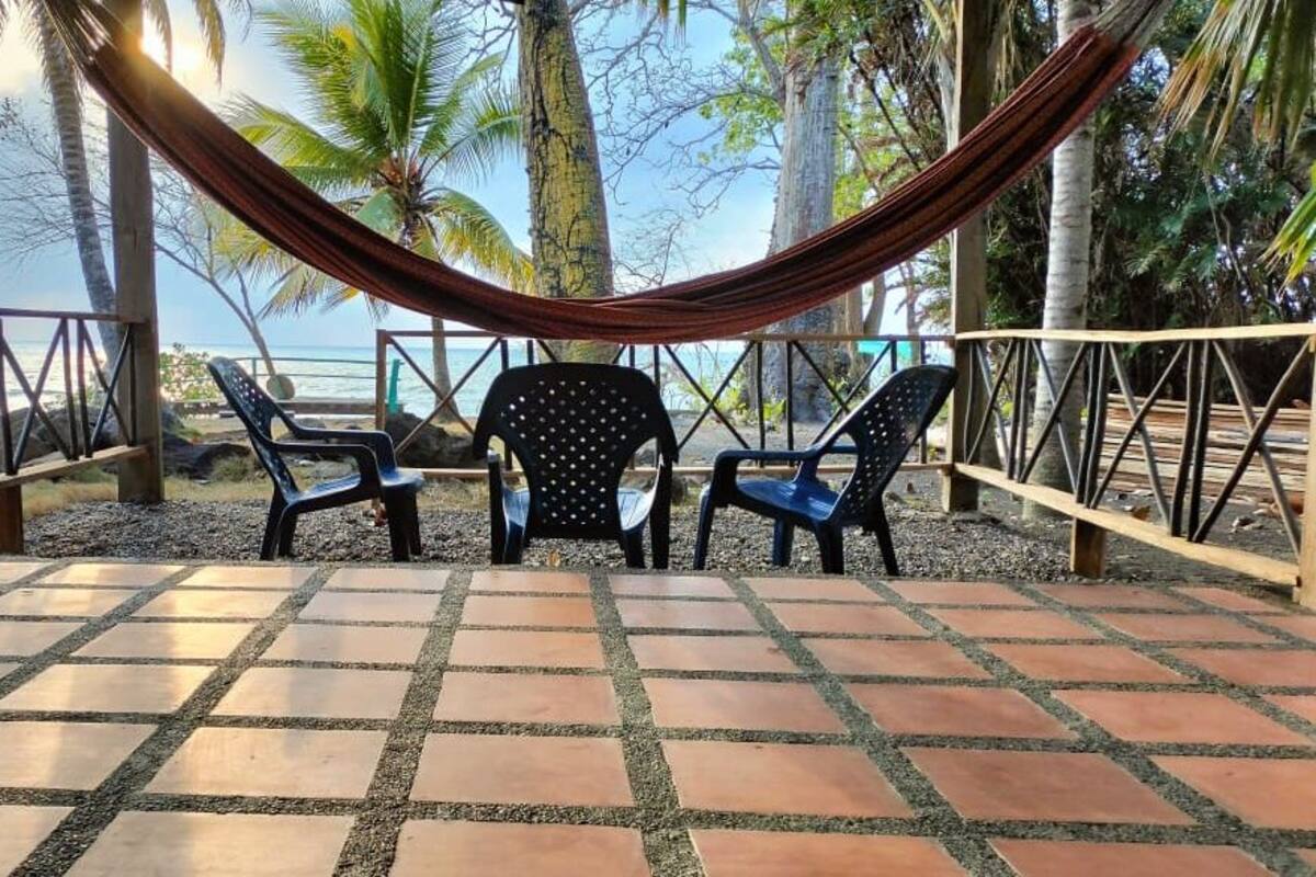 Una hamaca y dos sillas en un patio con baldosas y vista al océano.
