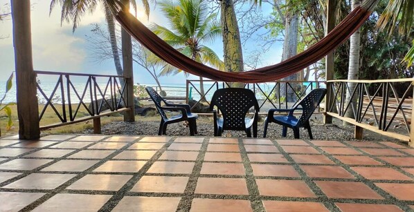 A hammock and two chairs on a tiled patio with a view of the ocean.