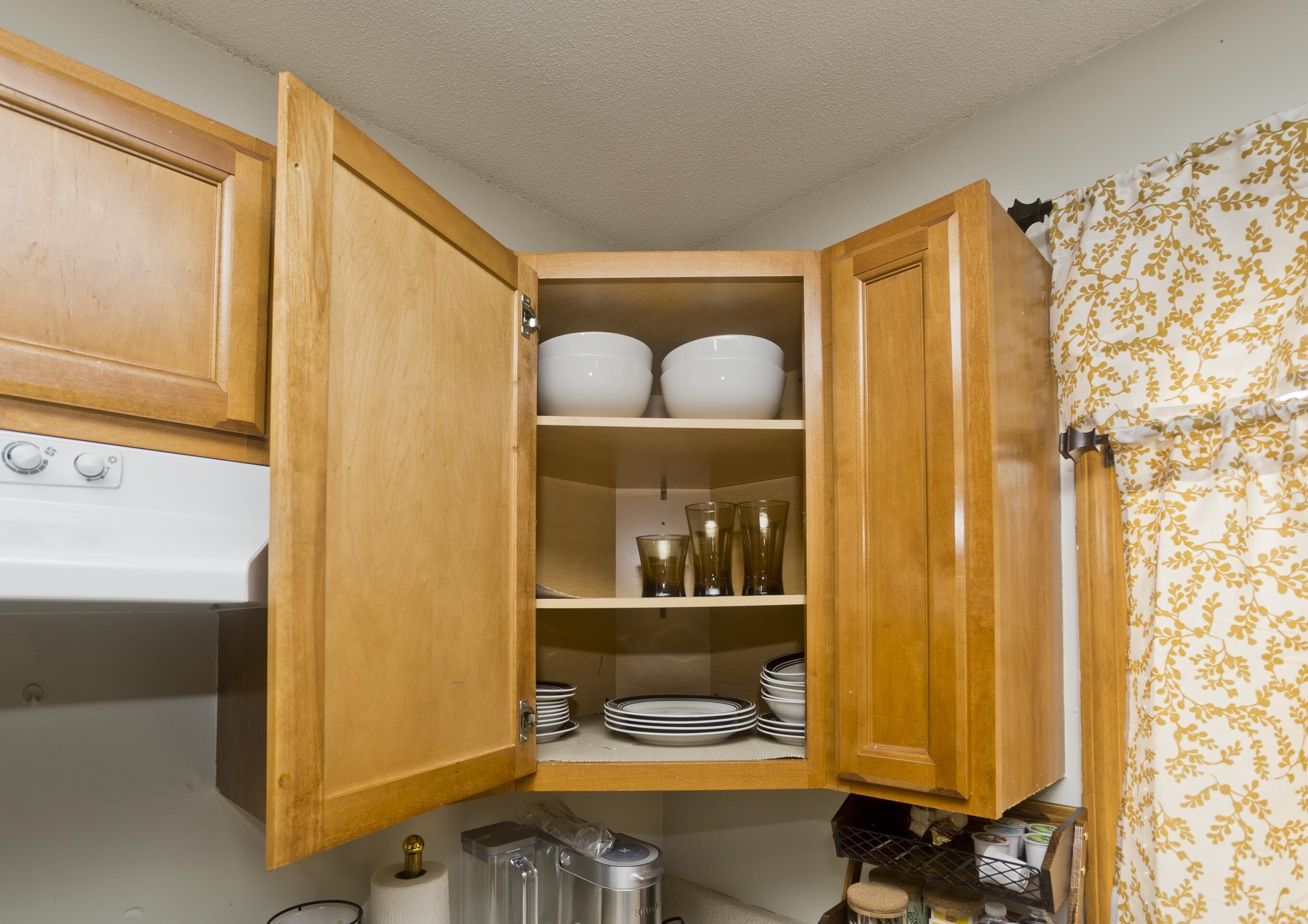 A kitchen with wooden cabinets, a stove, and shelves with bowls, glasses, and plates.