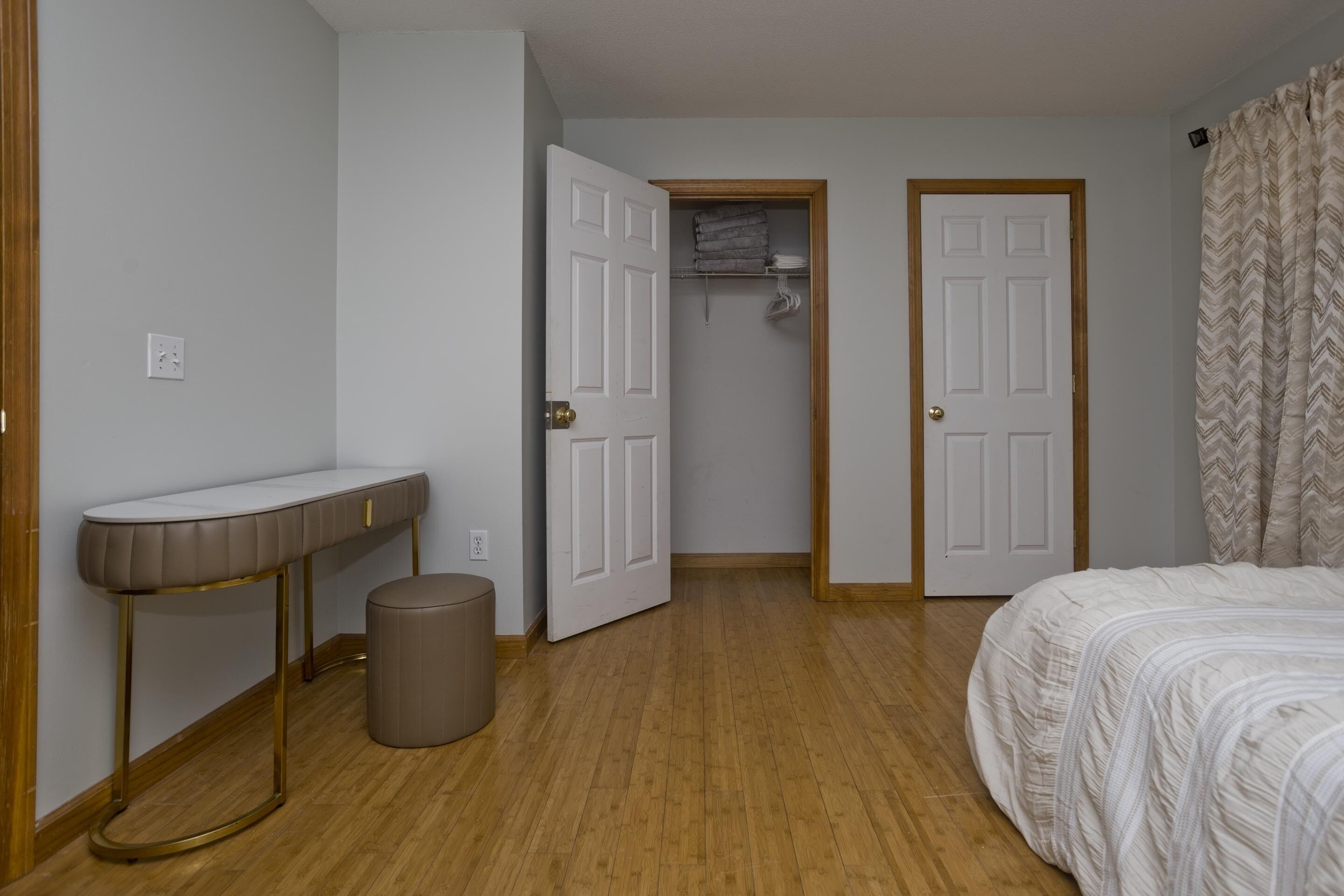A bedroom with a bed, a bedside table, a trash bin, and a closet with hanging clothes.