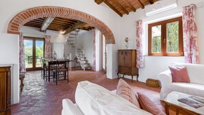 A spacious living area with a white sofa, a dining table with chairs, a staircase, and a wooden cabinet. - Private Villa with private pool, A/C, WIFI, TV, patio, panoramic view, close to Montepulciano (Scrofiano)