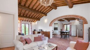 A spacious living area with a white sofa, a coffee table, and a dining table with chairs. There is a kitchen visible through an archway, and a refrigerator is seen in the background. - Private Villa with private pool, A/C, WIFI, TV, patio, panoramic view, close to Montepulciano (Scrofiano)