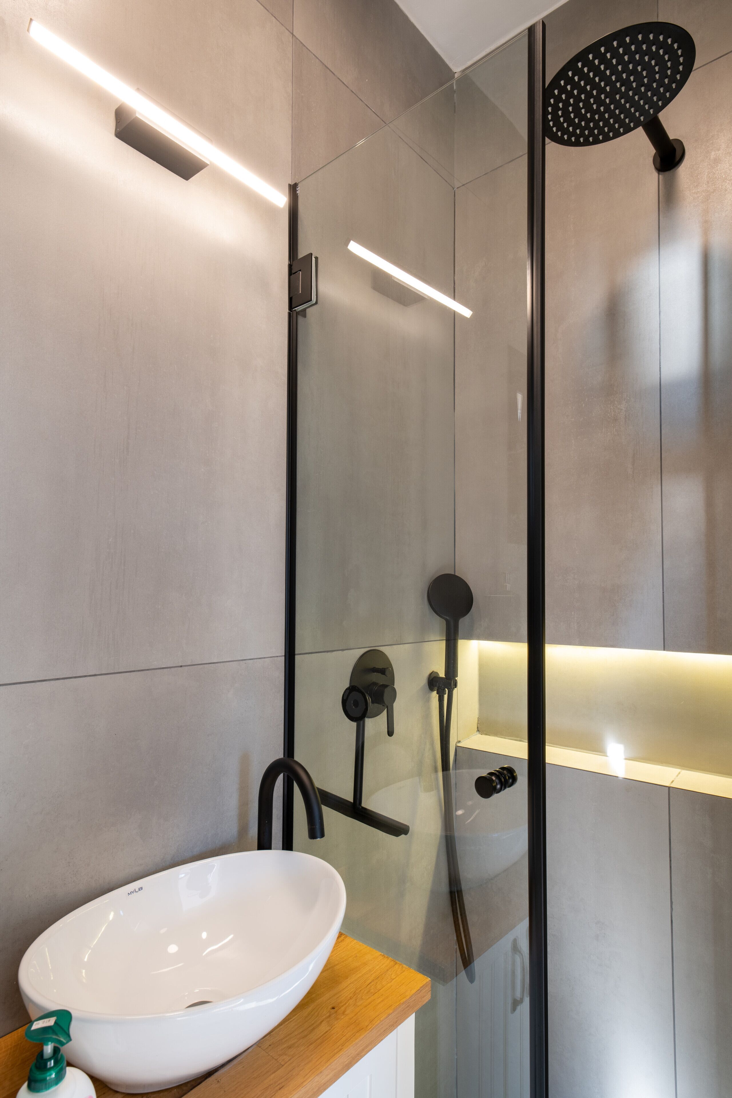 A modern bathroom with a white vessel sink, a handheld showerhead, and a glass-enclosed shower stall.