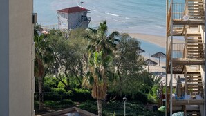 Un hôtel situé sur la côte, offrant une vue sur la mer, doté d’un balcon avec une balustrade et d’un espace de plage aménagé avec des parasols.