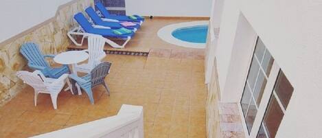 A rooftop terrace with a swimming pool, blue lounge chairs, and a white balustrade.
