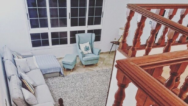 Una escalera con barandilla de madera que lleva a una sala de estar con un sofá y sillones.