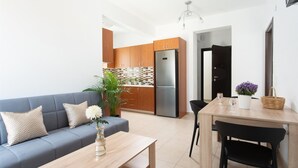 A modern kitchen with wooden cabinets, a stainless steel refrigerator, and a dining area with a table and chairs. - Tulipa Suites (Monemvasia)