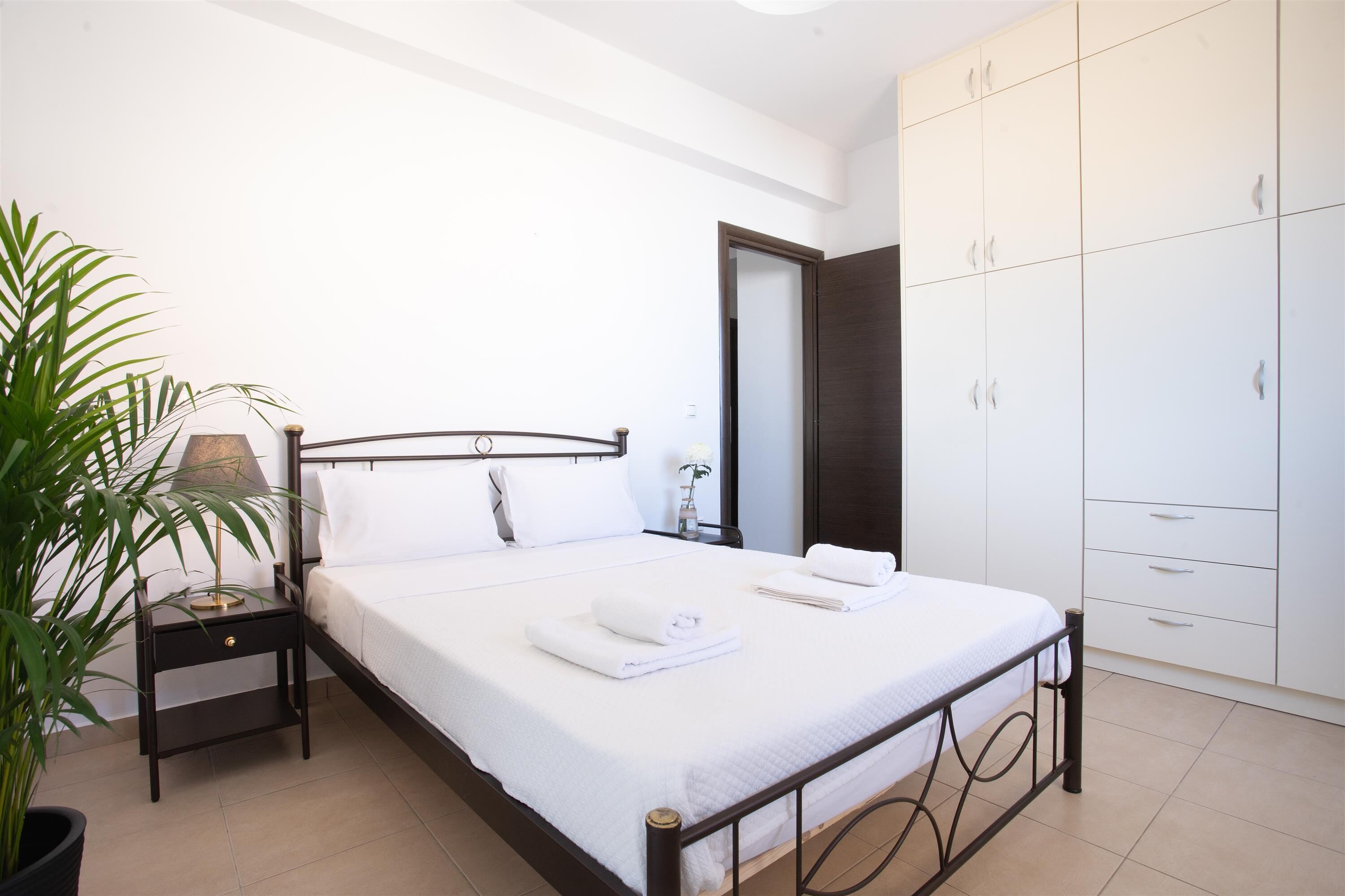 A bedroom with a bed, bedside table, lamp, potted plant, and wardrobe.