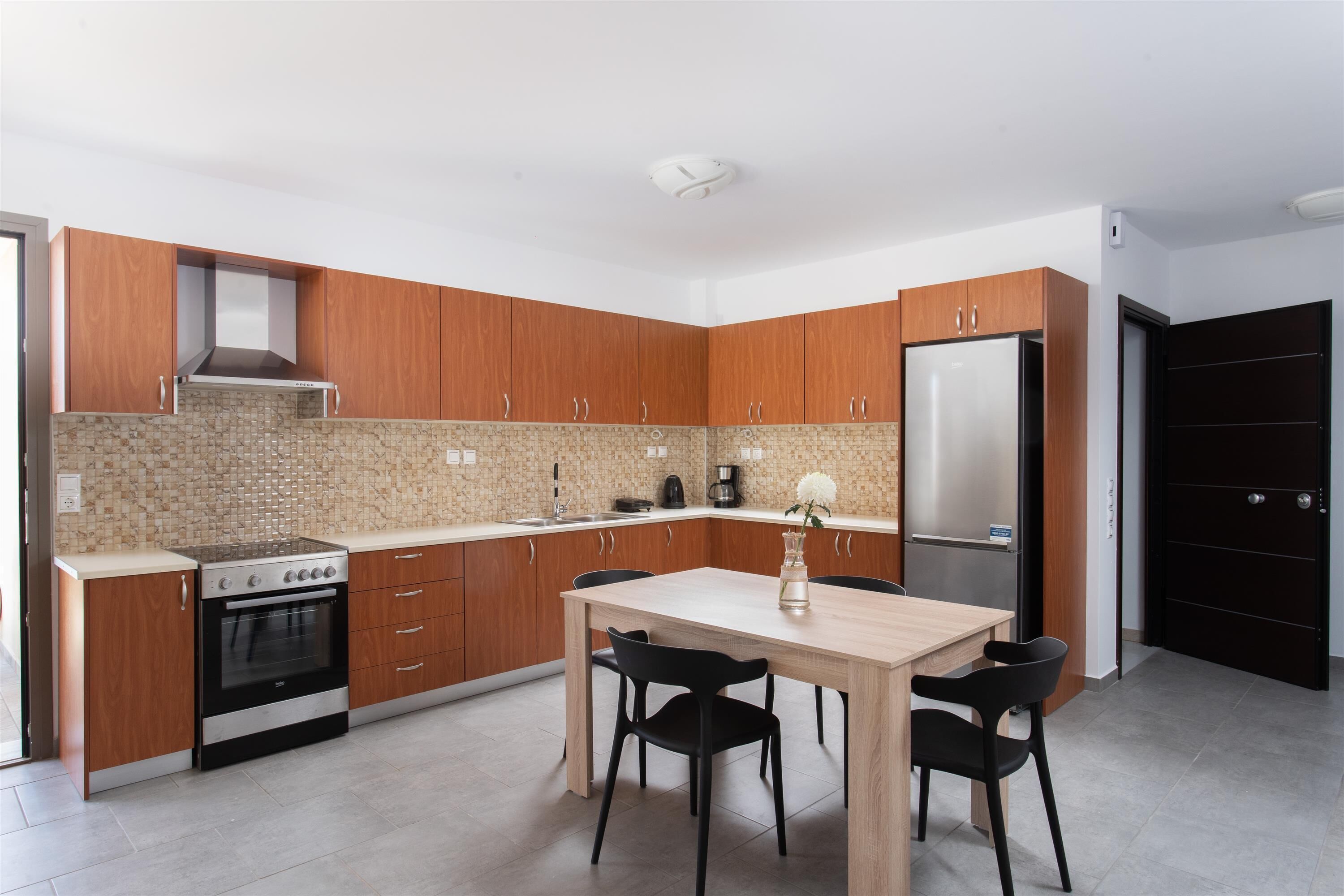 Una cocina moderna con armarios de madera, un refrigerador de acero inoxidable, un horno empotrado y una mesa de comedor con sillas.