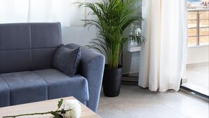 A modern living room with a grey sofa, a wooden coffee table with books, a potted plant, and a view of a mountainous landscape through a window. - Tulipa Suites (Monemvasia)