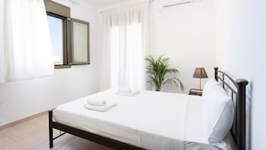 A clean, well-lit bedroom with a bed, curtains, a potted plant, and a bedside lamp. - Tulipa Suites (Monemvasia)