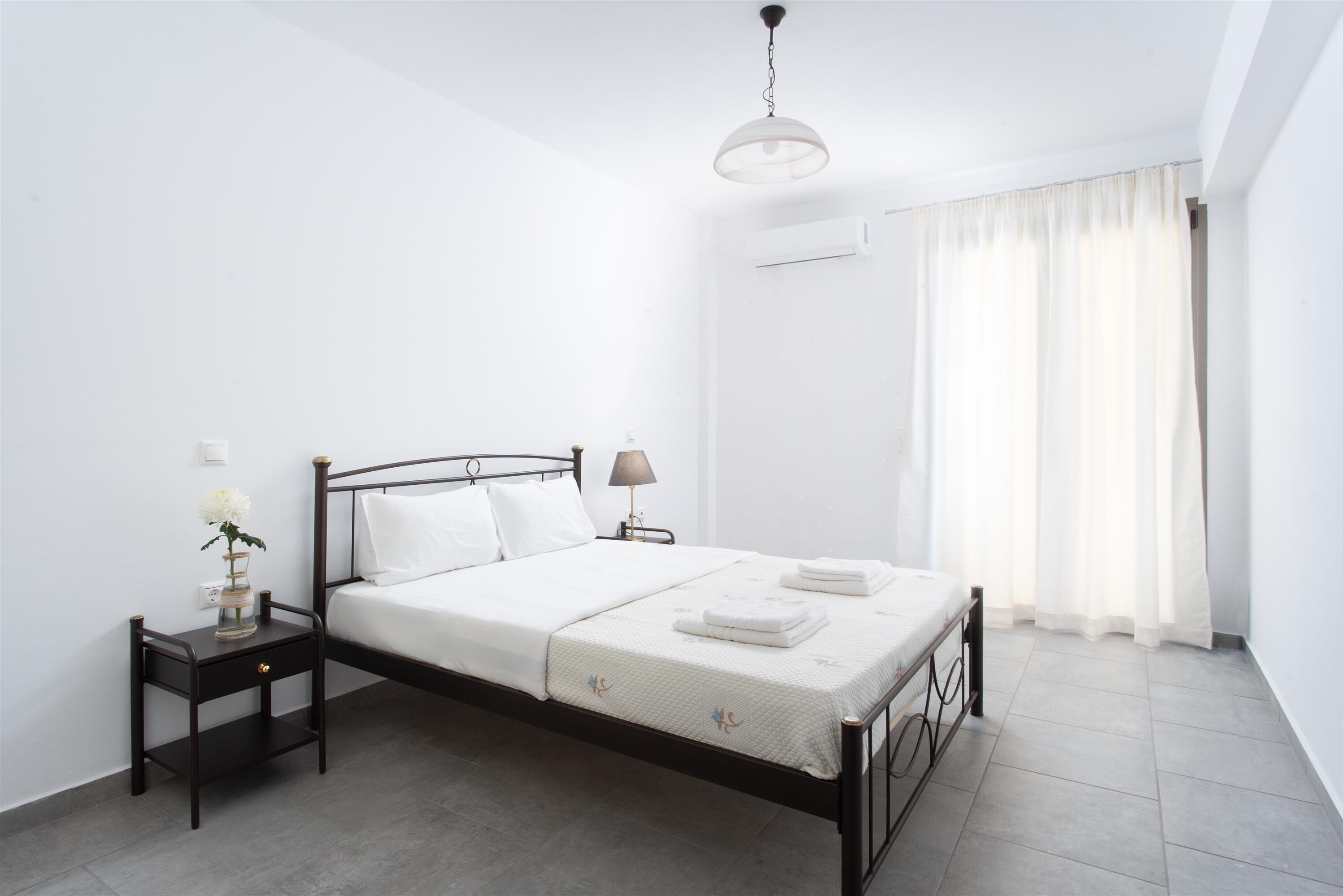 Un dormitorio con cama, mesita de noche, lámpara y ventana con cortinas.