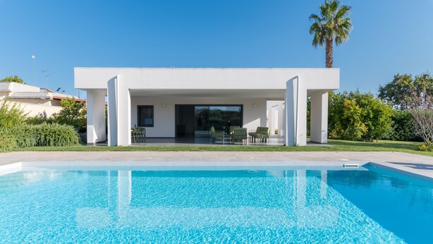 A modern house with a swimming pool, a covered patio, and a palm tree.