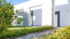 A modern building with a clean, white facade, a paved walkway, and a garden area with yellow flowers.