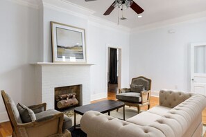 A living room with a white brick fireplace, a ceiling fan, and a framed picture on the wall.