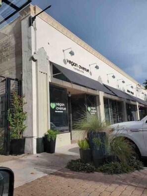A storefront with 'vegan avenue' signage, large windows, and potted plants in front.