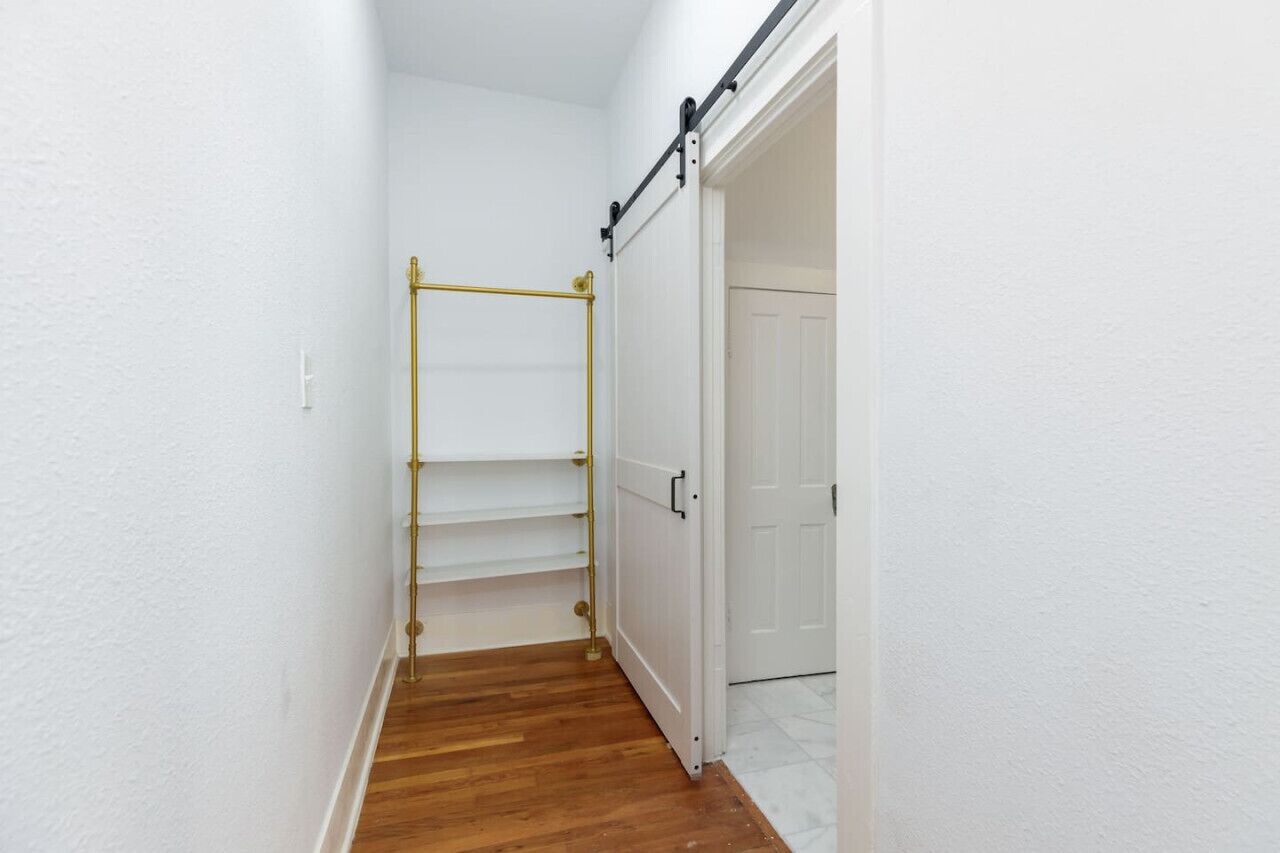 Un pasillo estrecho con suelo de madera, una puerta blanca y un perchero de metal.