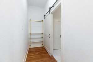 A narrow hallway with a wooden floor, a white door, and a metal rack.