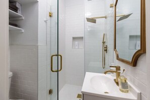 A modern bathroom with a glass-enclosed shower, a white sink with gold fixtures, and a large mirror.
