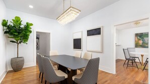 Un comedor moderno con una mesa rectangular, cuatro sillas, una planta grande en maceta y obras de arte enmarcadas en las paredes.