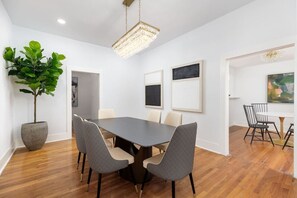 A modern dining room with a rectangular table, four chairs, a large potted plant, and framed artwork on the walls.