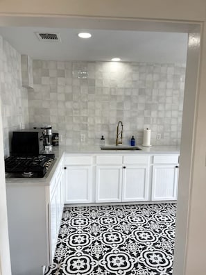 Una cocina con armarios blancos, estufa a gas, pileta con grifo y piso estampado.