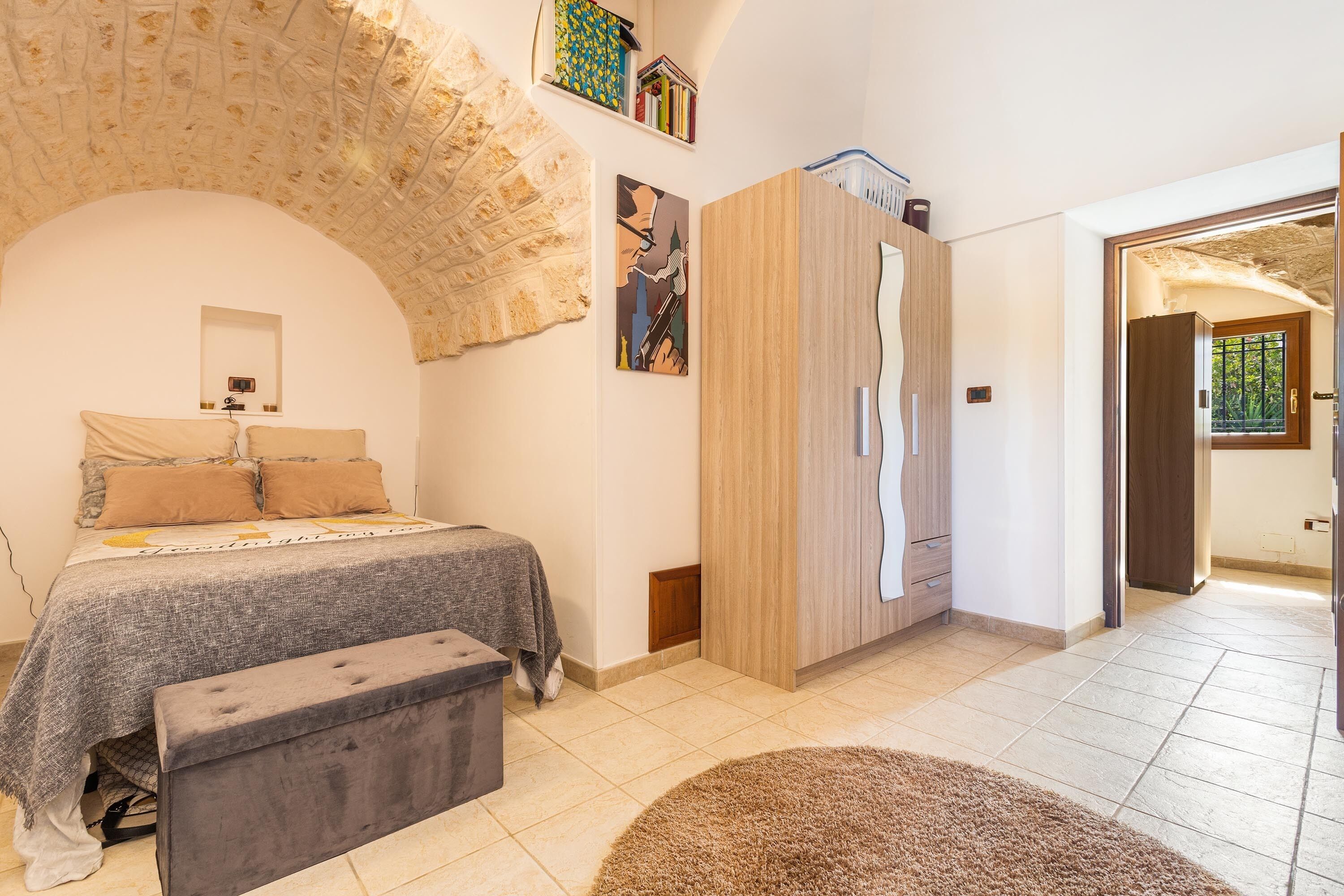 A bedroom with a bed, a bench, a wardrobe, and a door leading to another room.