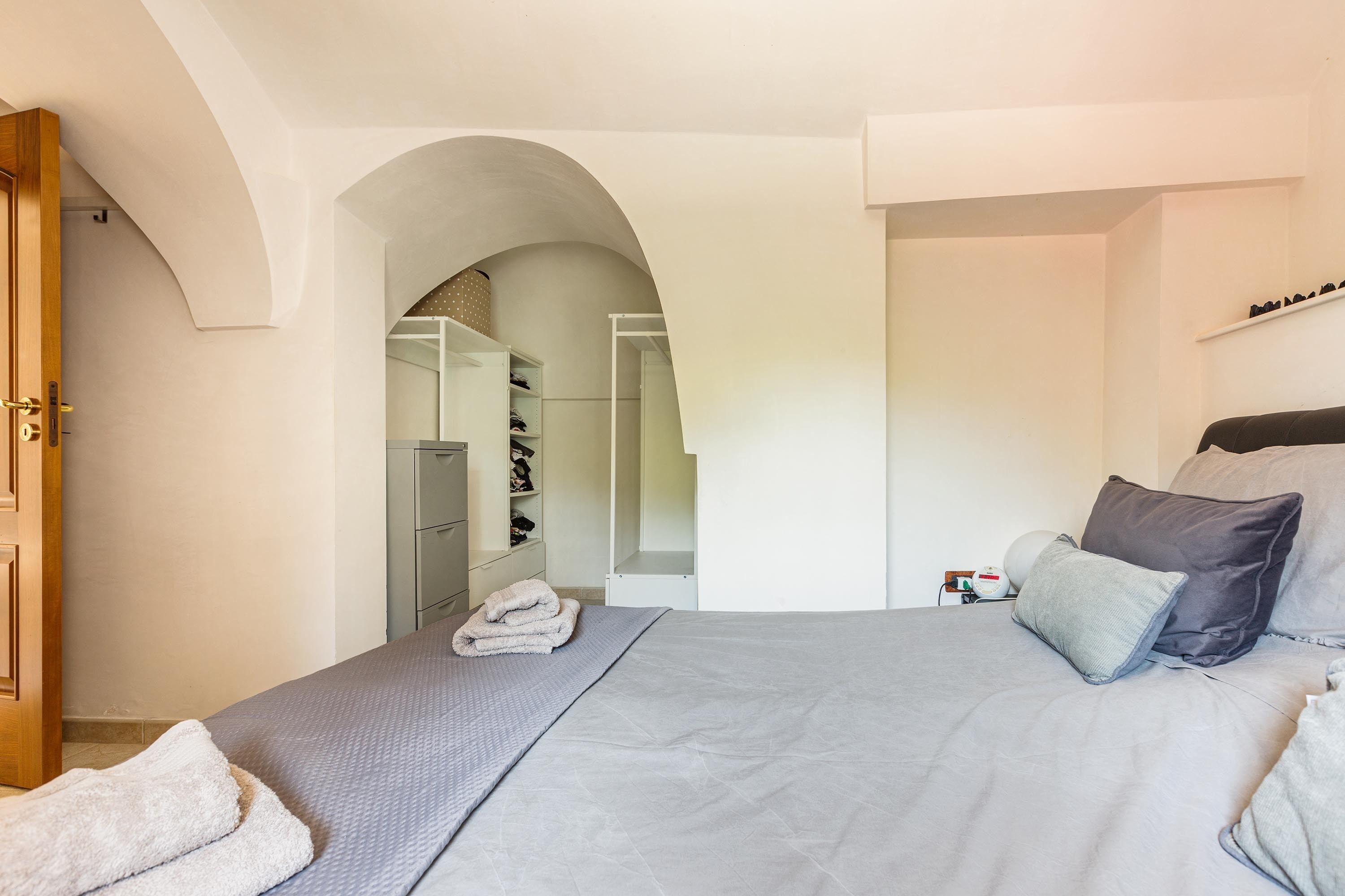 A bedroom with a bed, a wooden door, a closet, and an arched doorway leading to another room.