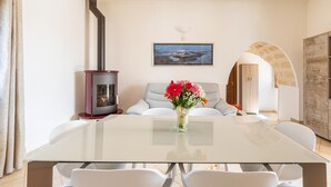 A modern dining room with a glass table, white chairs, a vase of flowers, a fireplace, and a framed picture on the wall. - 2942 Villa Cucunci by Barbarhouse (Ostuni)