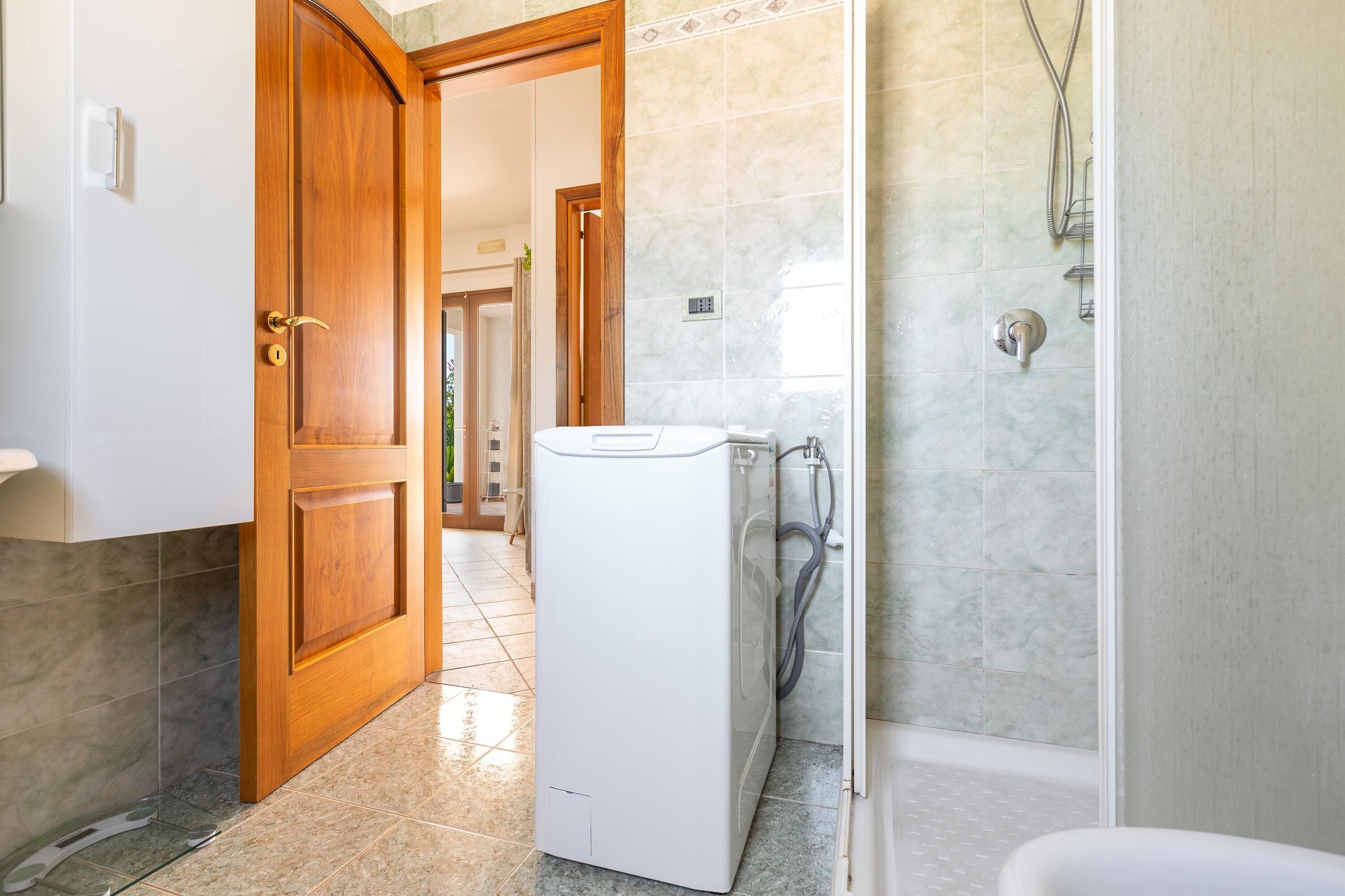 Ein Badezimmer mit einer weißen Waschmaschine, einer Dusche und einer Holztür.