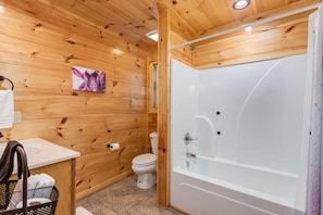 A wooden interior bathroom with a white bathtub, a toilet, and a sink. - Family Cabin w/ Game Room In Heart Of Pigeon Forge (Pigeon Forge)