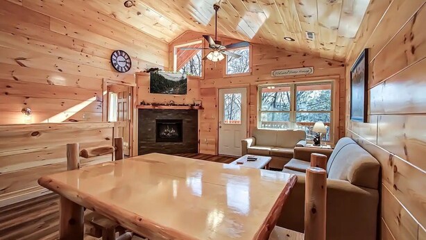 A cozy cabin interior with a wooden interior, a fireplace, a dining table, and a sofa. - Family Cabin w/ Game Room In Heart Of Pigeon Forge (Pigeon Forge)