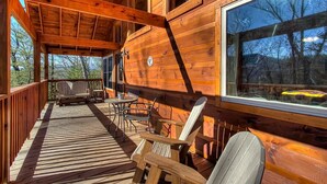A wooden deck with a covered seating area, large windows, and a view of trees. - Family Cabin w/ Game Room In Heart Of Pigeon Forge (Pigeon Forge)