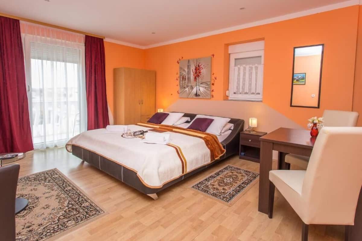 Ein Hotelzimmer mit einem großen Bett, einem Schreibtisch, einem Stuhl, einem Kleiderschrank und einem Fenster mit Vorhängen.