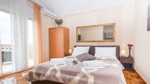 Hotellihuone, jossa on suuri sänky, puinen vaatekaappi, peili, yöpöytä lampun kanssa ja ikkuna, jossa on verhot.