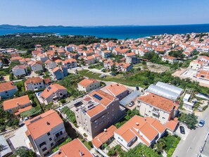 Une vue aérienne d’un quartier résidentiel situé sur la côte, avec des maisons, des routes et une vue dégagée sur la mer.