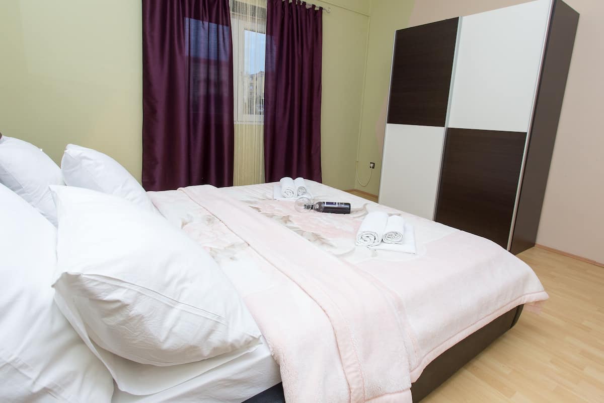 Ein ordentlich bezogenes Bett mit weißer und rosa Bettwäsche, ein Nachttisch mit Fön und ein Schrank mit Karomuster.