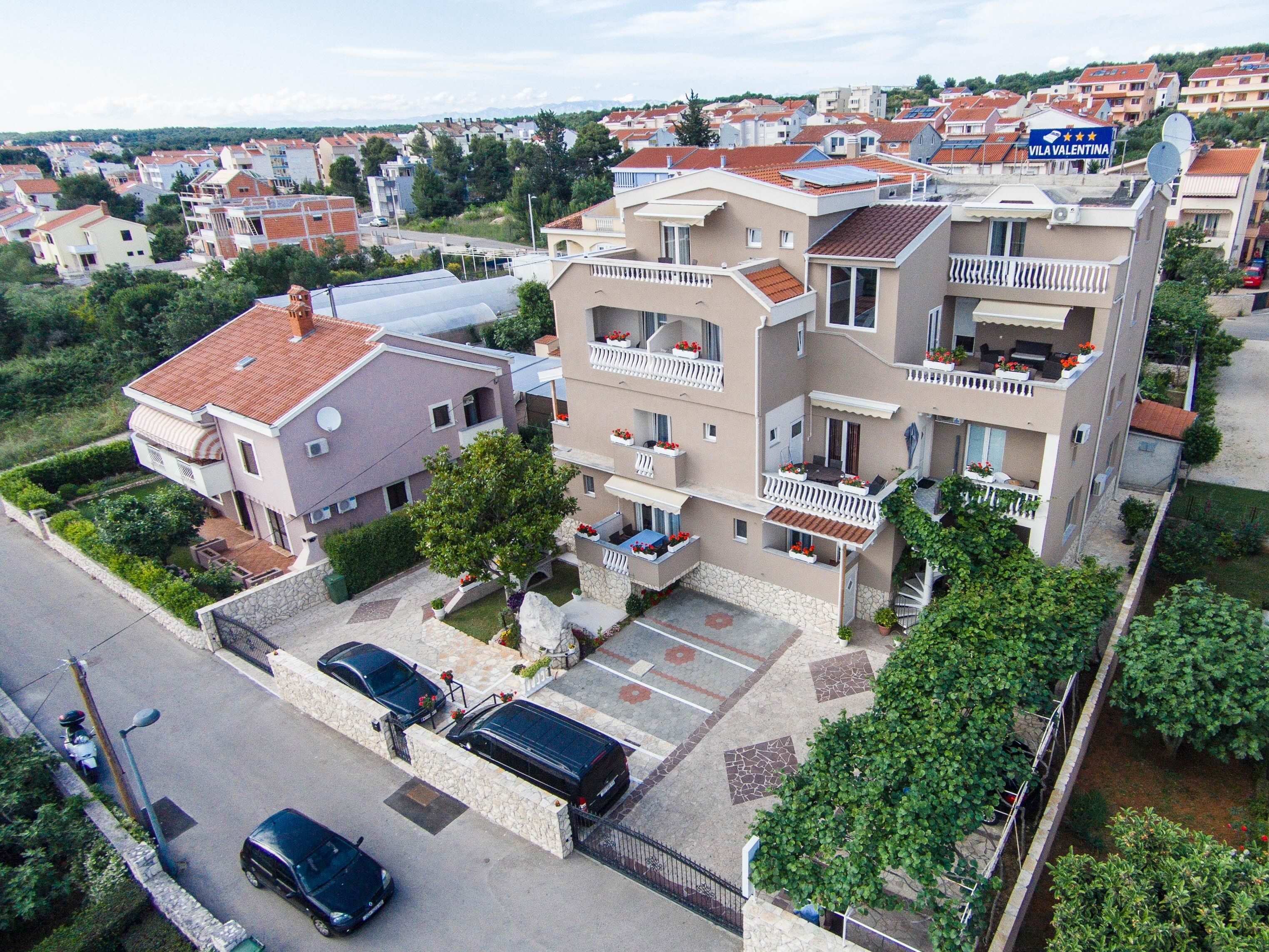 A multi-story residential building with balconies, a parking area, and a view of surrounding houses.