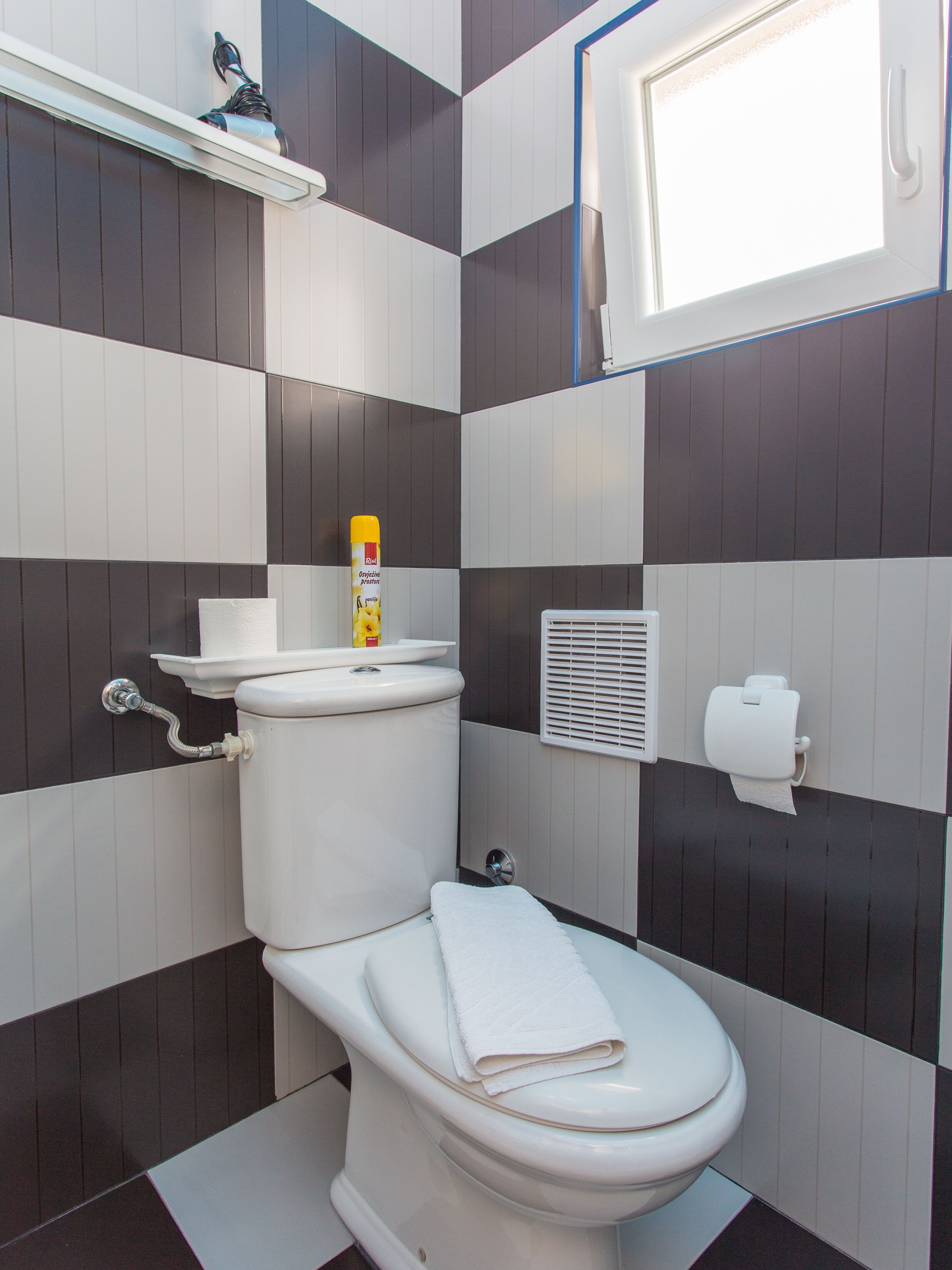 A bathroom with a toilet, a towel, a toilet paper holder, and a window.