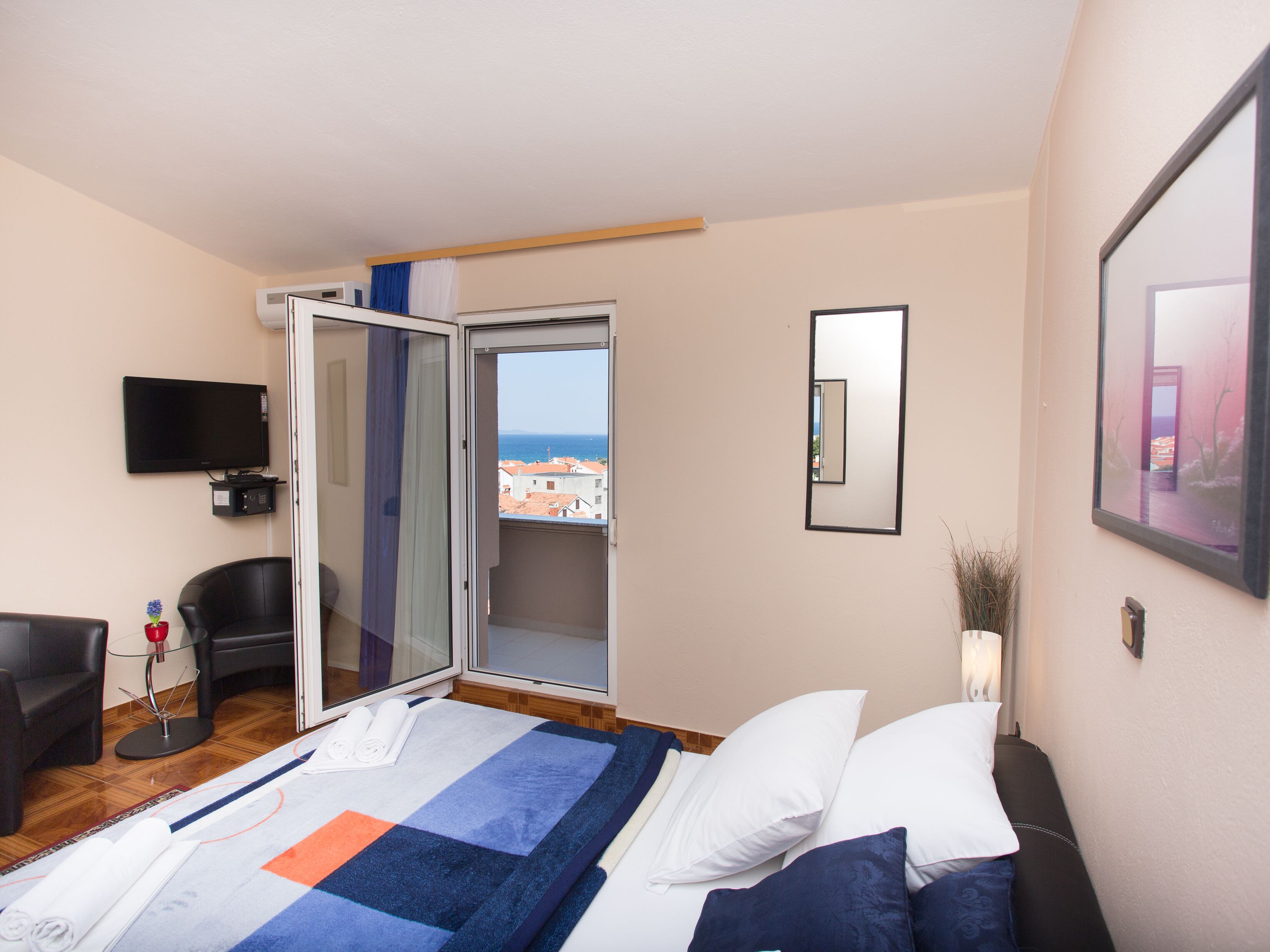 Habitación de hotel con cama, televisión, sillón y vista al mar por una puerta abierta.