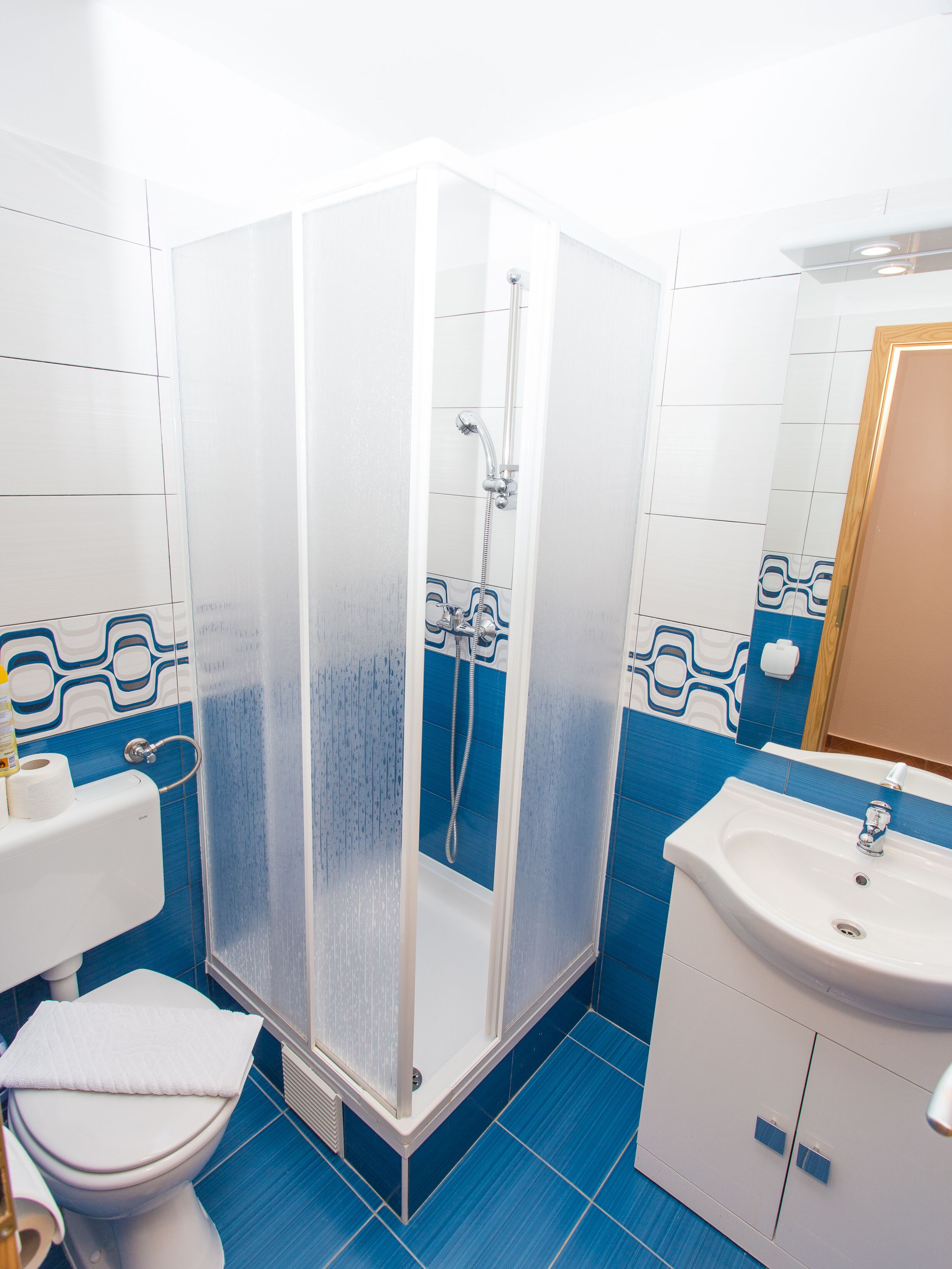 Ein Badezimmer mit Duschkabine, Toilette, Waschbecken und blauen Fliesen.