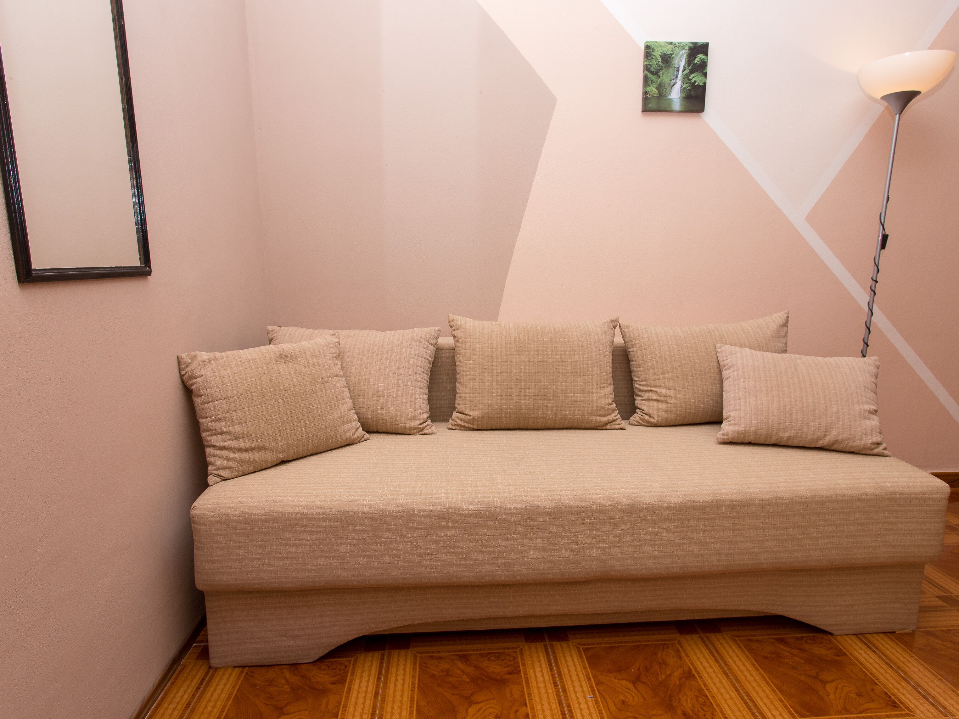 A sofa with four cushions in a room with wooden flooring and a wall-mounted picture.