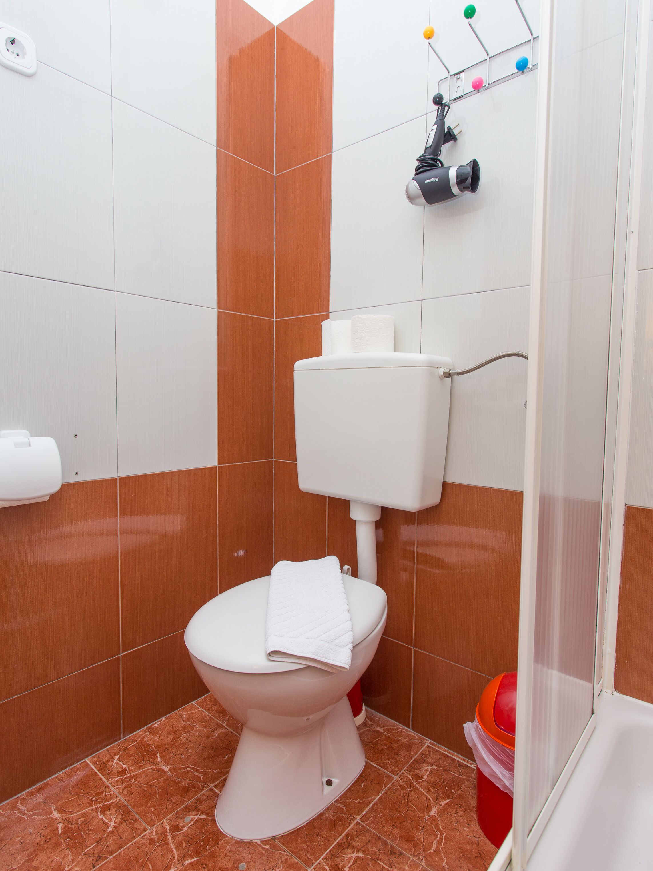 Ein Badezimmer mit einer weißen Toilette, einem Handtuch auf der Sitzfläche, einem Handtrockner und einer roten Mülleimer.