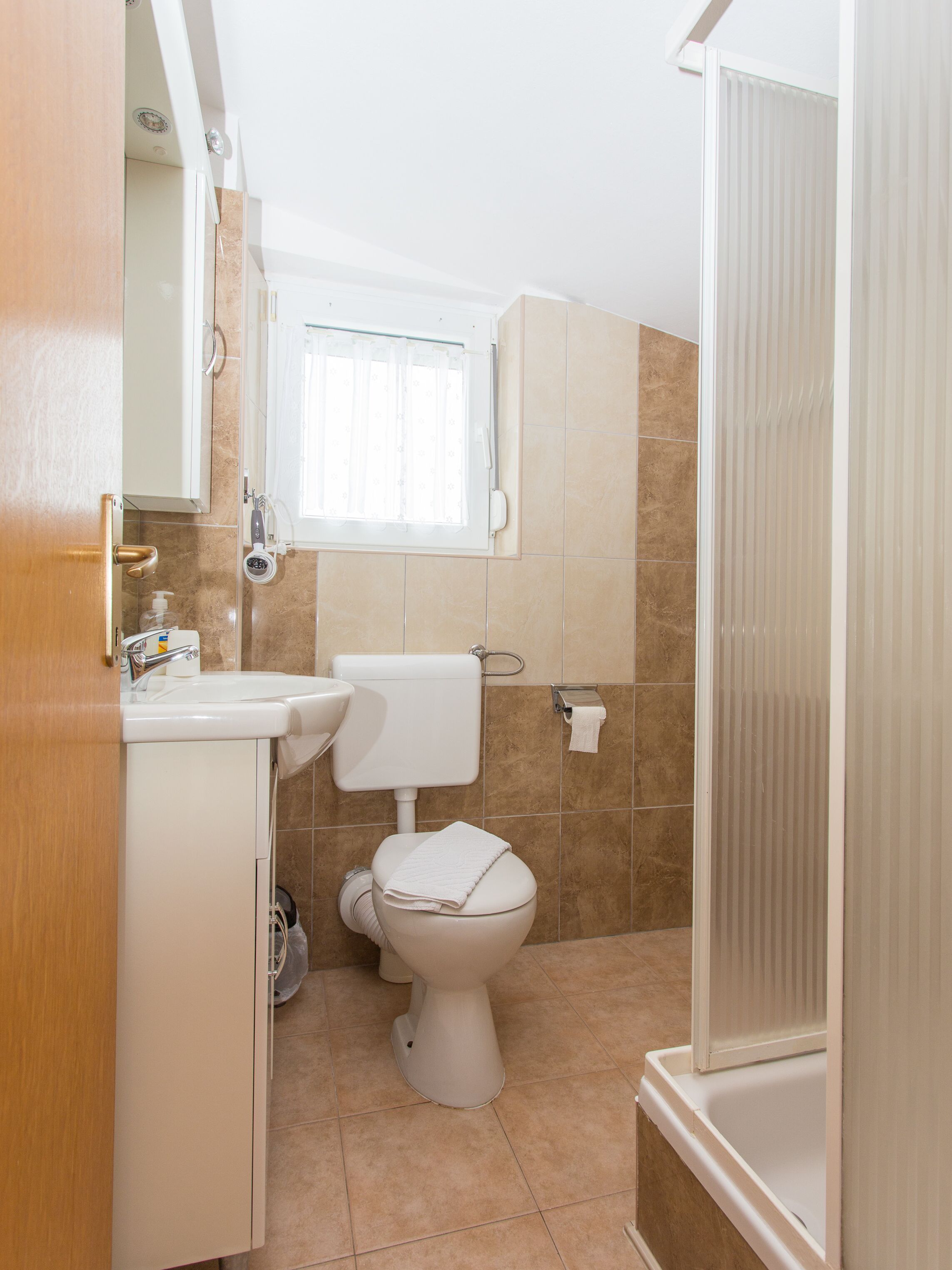 A bathroom with a toilet, sink, and window.