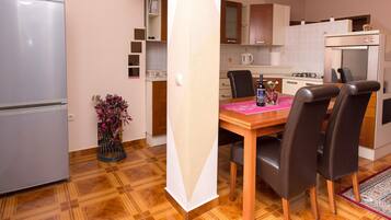 A compact kitchen with a dining table, chairs, a refrigerator, and a coffee machine.