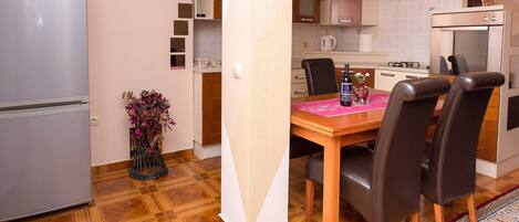 A compact kitchen with a dining table, chairs, a refrigerator, and a coffee machine.
