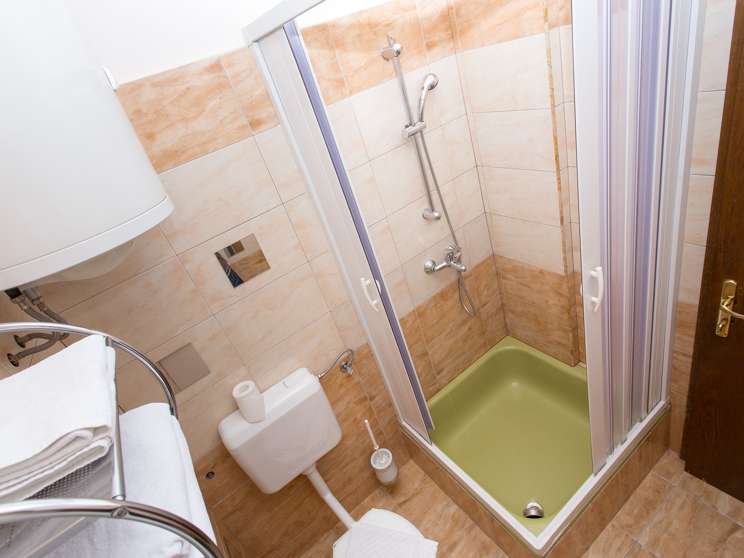 A bathroom with a shower, toilet, sink, and a green bathtub.
