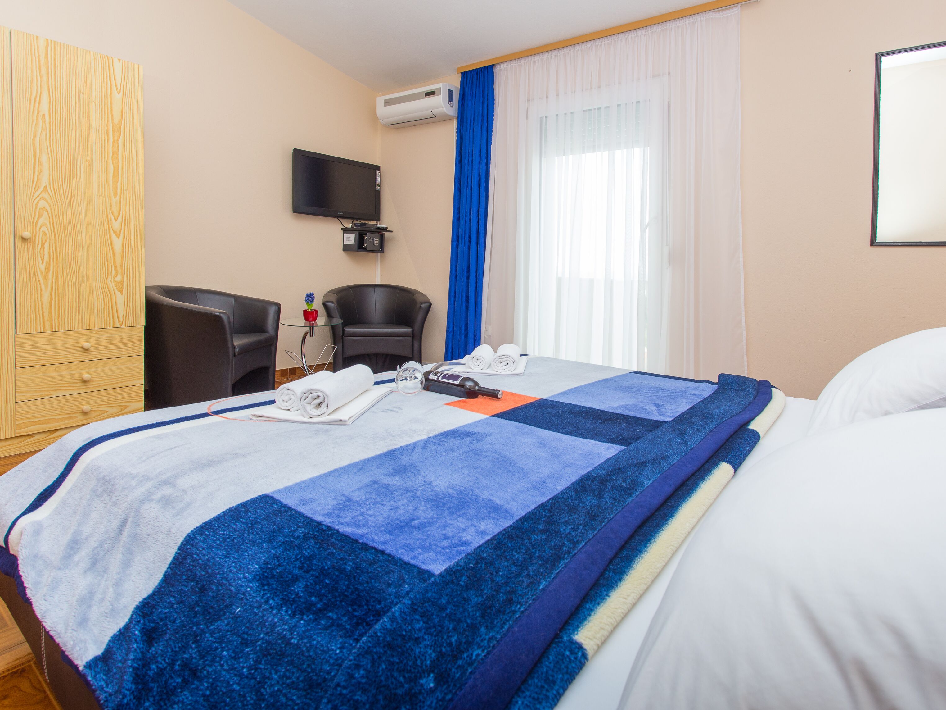 A hotel room with a bed, a desk, a chair, a TV, and a window with curtains.