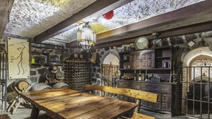 A rustic cellar with wooden furniture, stone walls, and various wine barrels.
