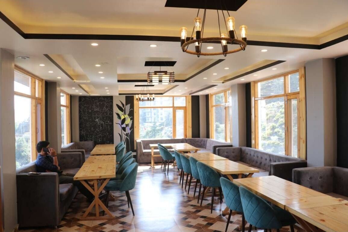 A modern restaurant with high ceilings, large windows, and a mix of seating options including tables and booths.